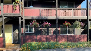 A two-story building with a balcony, a flower bed with various flowers, and a door marked with the number 2. - Hidden JEM Apartment-Hotel - Spacious Home Away From Home (Coal Harbour)
