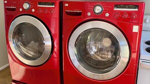Two red LG Direct Drive front-loading washing machines in a kitchen with white cabinets. - Hidden JEM Apartment-Hotel - Spacious Home Away From Home (Coal Harbour)