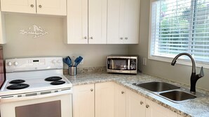 A kitchen with white cabinets, a stove, a microwave, and a sink. - Hidden JEM Apartment-Hotel - Spacious Home Away From Home (Coal Harbour)