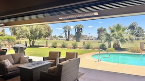 Eine Terrasse mit Korbmöbeln, einem Pool und Blick auf einen Golfplatz.