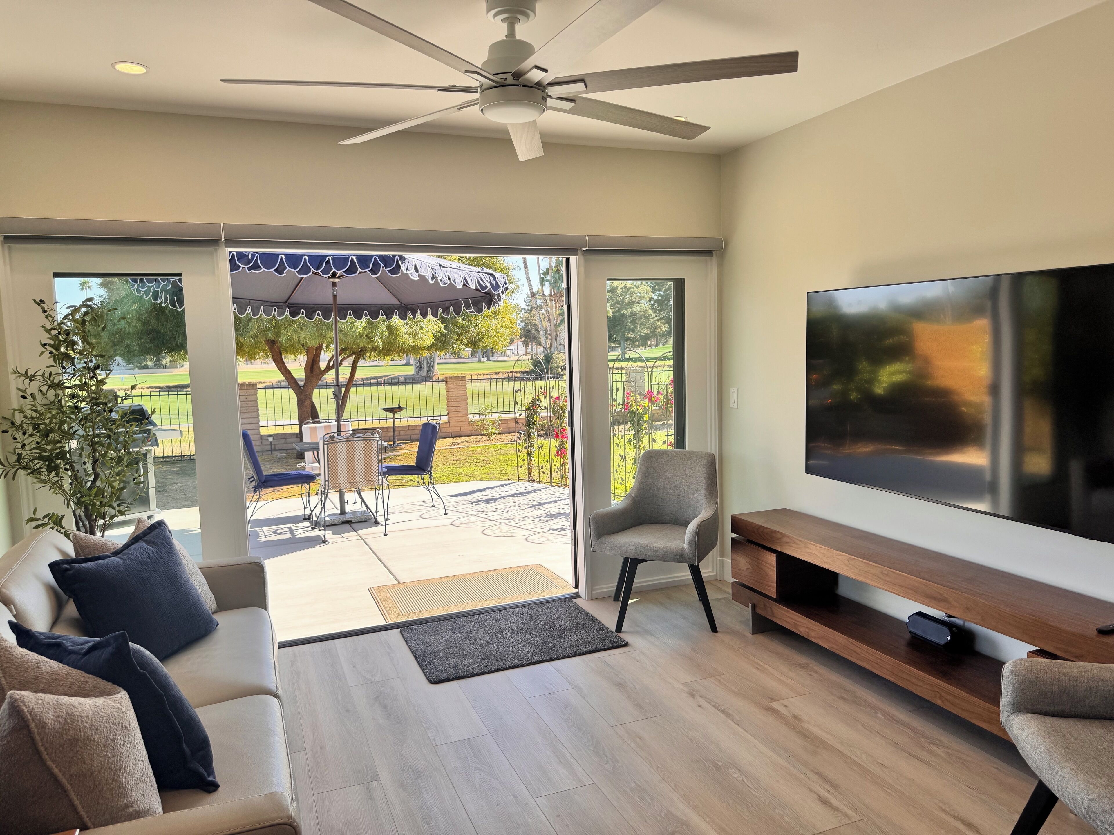 Een moderne woonkamer met een grote televisie, comfortabele zithoek en een terras met tuinmeubilair.