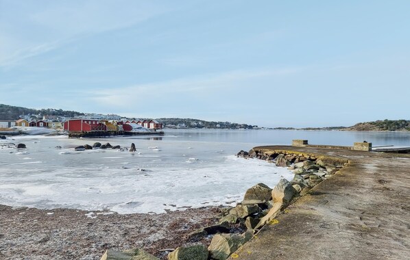 A coastal scene with a frozen water body, a stone breakwater, and a row of colorful buildings in the background.