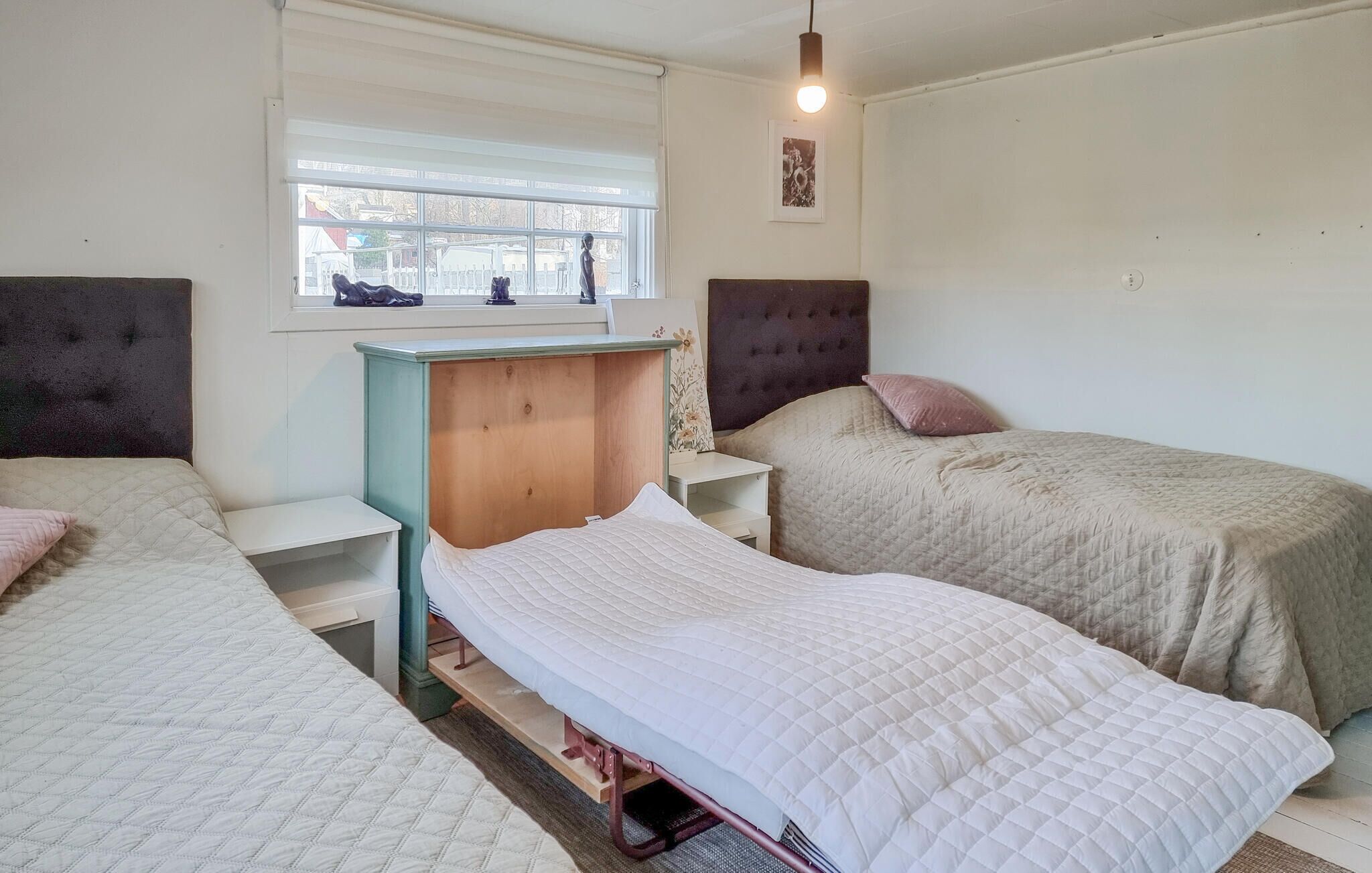 A bedroom with two beds, a window, and a wall-mounted light fixture.