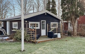 A small, dark wooden cabin with a porch, a ladder, and outdoor seating.