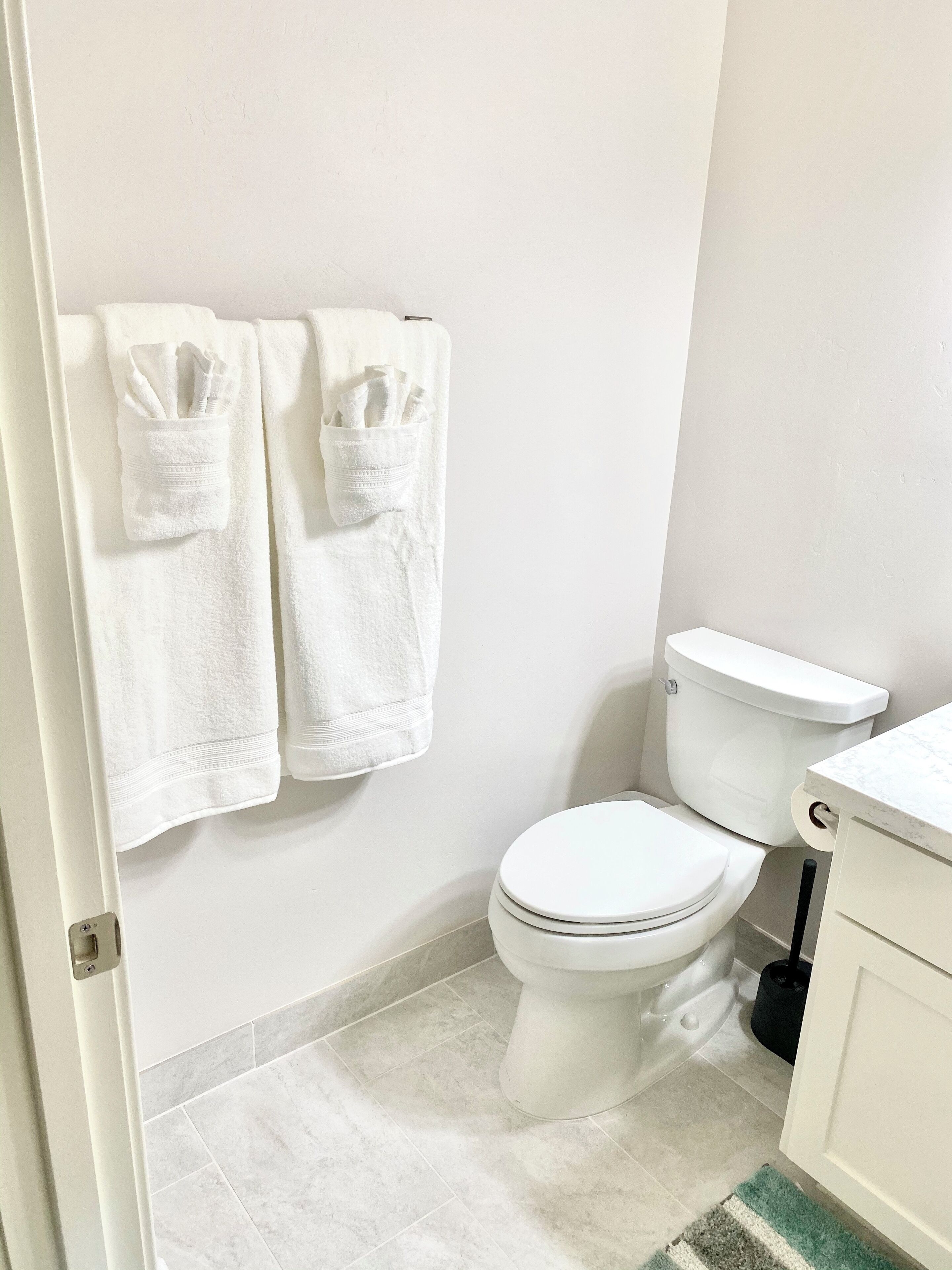 Ein Badezimmer mit zwei weißen Handtüchern an der Wand, einer weißen Toilette und einem weißen Waschbecken mit Marmorplatte.