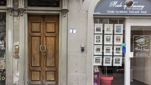 Um edifício com porta dupla de madeira, placa com o número 7 e vitrine exibindo quadros emoldurados.