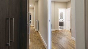 Um corredor com piso de madeira, um guarda-roupa de madeira escura e uma porta branca que dá para o banheiro.