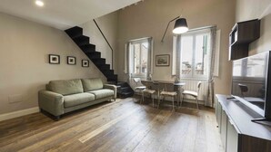Sala de estar com sofá, mesa de jantar, cadeiras, escada e área de cozinha.