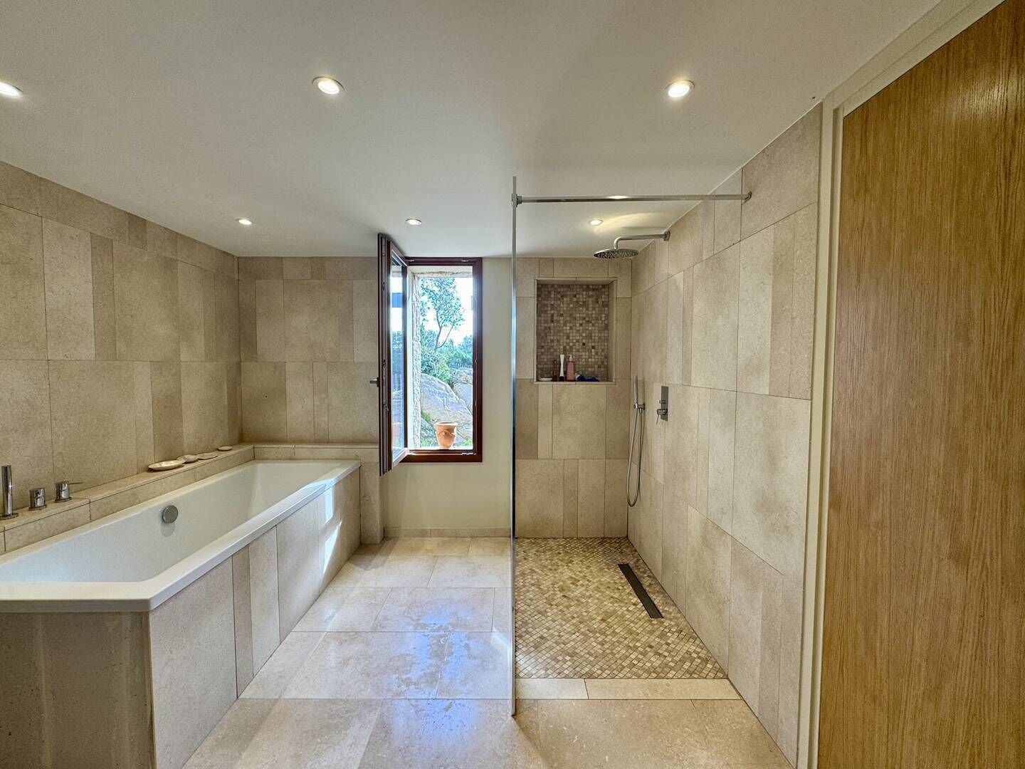 Une salle de bain moderne équipée d’une baignoire, d’une douche et d’une fenêtre donnant sur l’extérieur.