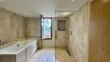 Une salle de bain moderne équipée d’une baignoire, d’une douche et d’une fenêtre donnant sur l’extérieur.