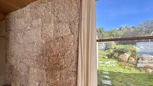 Una habitación con pared de piedra y vista a un jardín con un estanque y piedras.