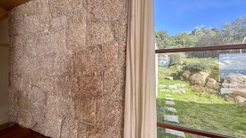 Une pièce avec un mur en pierre et une vue sur un jardin agrémenté d’un bassin et de pierres plates servant de pas.
