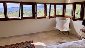 Una habitación con cama, una silla y vistas al mar a través de amplios ventanales.