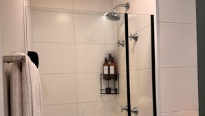 A glass-enclosed shower with a handheld showerhead, a towel rack, and a small shelf with toiletries. - Studio Brooklin 1min from the subway and close to the consulate (Brooklin São Paulo)