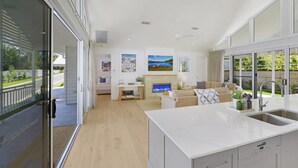 A modern kitchen with a large island, a dining area with a sofa and a fireplace, and a view of the outdoors through large windows.