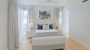 A bedroom with a bed, two bedside tables, a nightstand, a ceiling fan, and a framed picture on the wall.