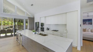 A modern kitchen with white cabinetry, a large island, and a dining area with a view of the garden.