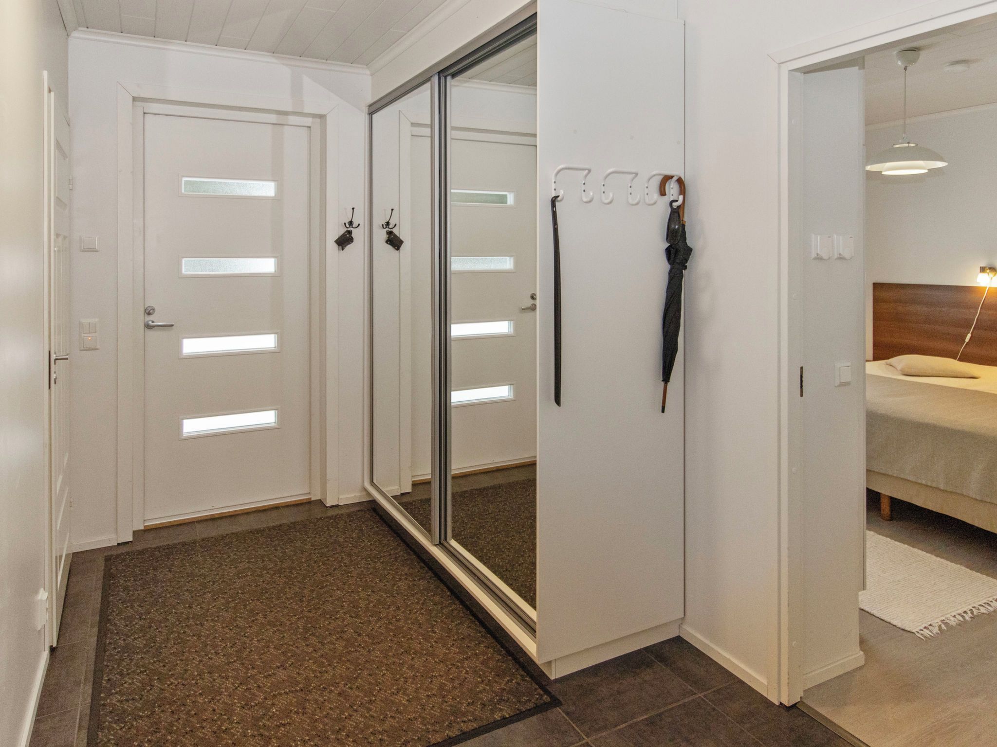 Ein Flur mit Teppichboden, einer Spiegeltür zum Kleiderschrank und einem Bett mit Kopfteil und Nachttischlampe.