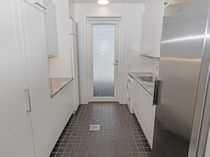 A narrow kitchen with white cabinets, a stainless steel refrigerator, and a tiled floor.