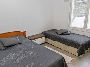 A bedroom with two single beds, a wooden headboard, a nightstand, a small drawer unit, and a window with blinds.