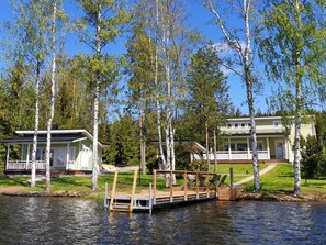A lakeside property with a dock, a covered deck, and two main buildings with attached porches.