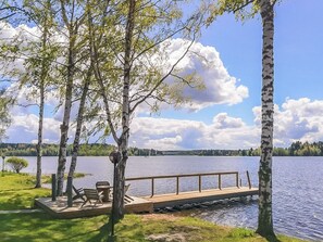 A lakeside deck with a wooden railing, a bench, and a table, surrounded by birch trees.