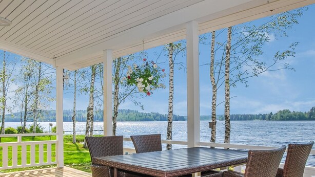 Un espace extérieur abrité, doté d’une table et de chaises, qui offre une vue sur une étendue d’eau et est entouré d’arbres.