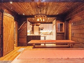Un intérieur rustique en bois, avec un coin repas, une cuisine visible à travers une porte ouverte et un escalier.