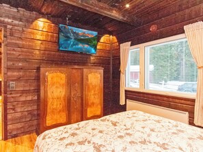 A room with wooden walls, a bed with a floral bedspread, a mounted TV, and a window with curtains. - Vacation home Jauli by Interhome (Ikaalinen)