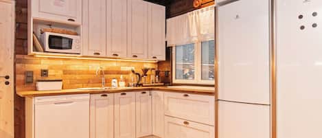 A kitchen with wooden cabinets, a microwave, a refrigerator, and a window with blinds.