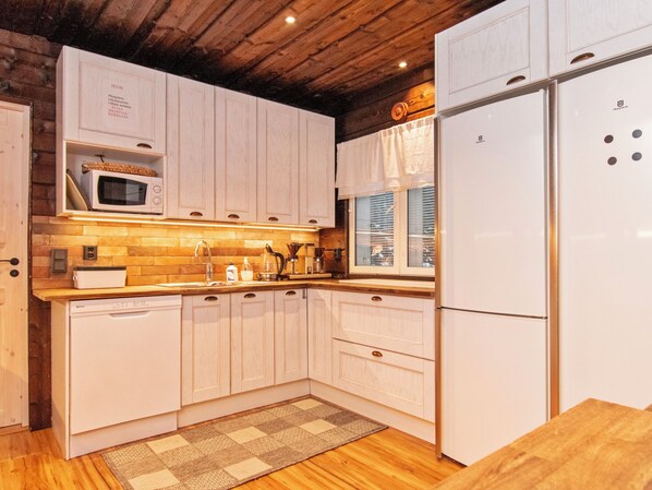 A kitchen with wooden cabinets, a microwave, a refrigerator, and a window with blinds.