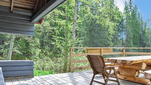 Une terrasse en bois avec une table et des chaises, donnant sur une zone boisée.
