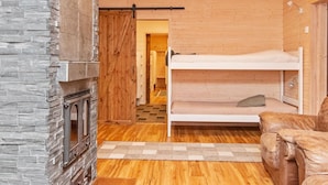 Une pièce chaleureuse avec une cheminée en pierre, des murs en bois, un lit superposé et un canapé en cuir.