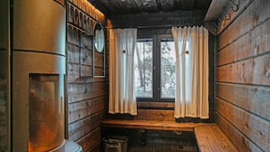 L’intérieur d’une cabine avec un banc en bois, une fenêtre avec des rideaux, un miroir et une poubelle.