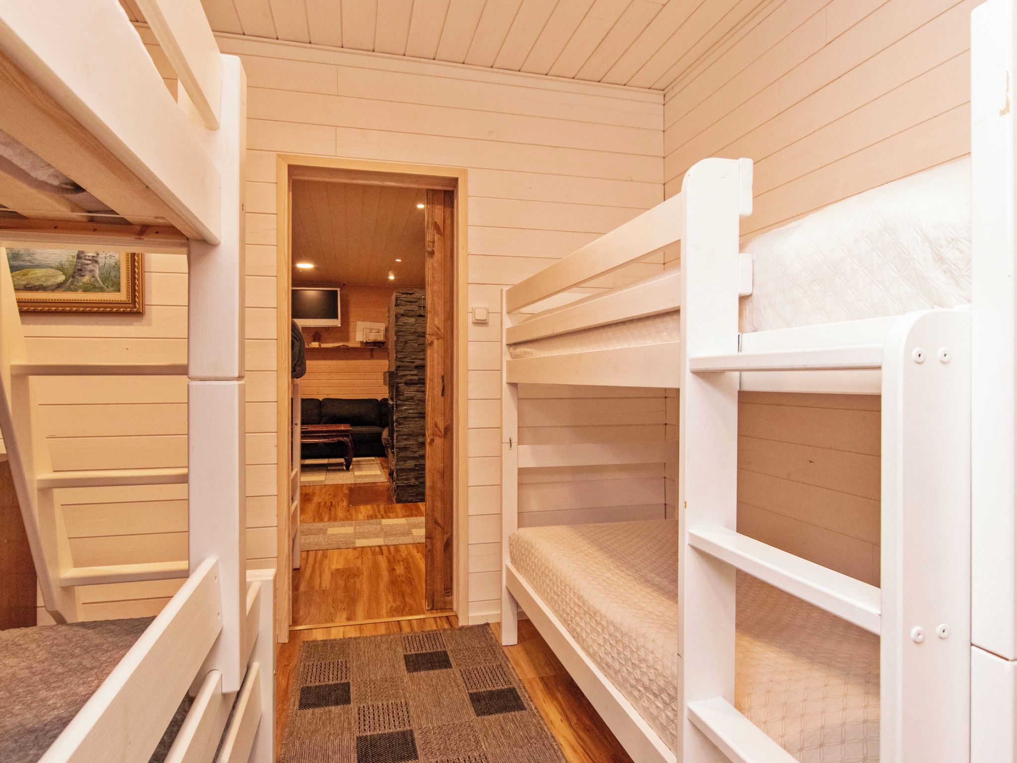 A bunk bed room with a wooden floor and a small kitchen area visible through an open door.