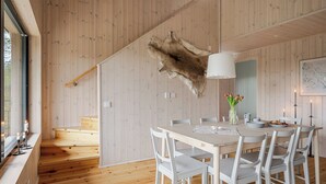 A modern interior with wooden walls, a dining area with white chairs, a fur coat hanging, and a map on the wall.