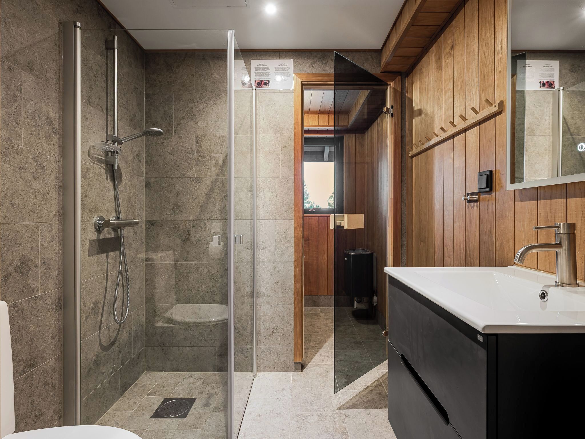 A modern bathroom with a glass-enclosed shower, a vanity with a sink and mirror, and wooden paneling on the walls.