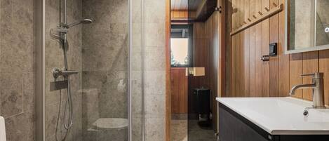 A modern bathroom with a glass-enclosed shower, a vanity with a sink and mirror, and wooden paneling on the walls.