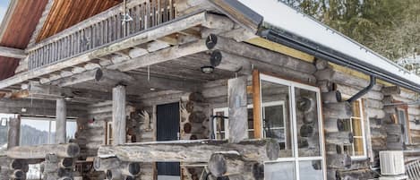 Una cabaña de troncos con balcón, ventanas amplias y chimenea.