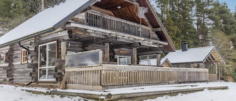 Una cabaña de madera con balcón, terraza de madera y alrededores nevados.