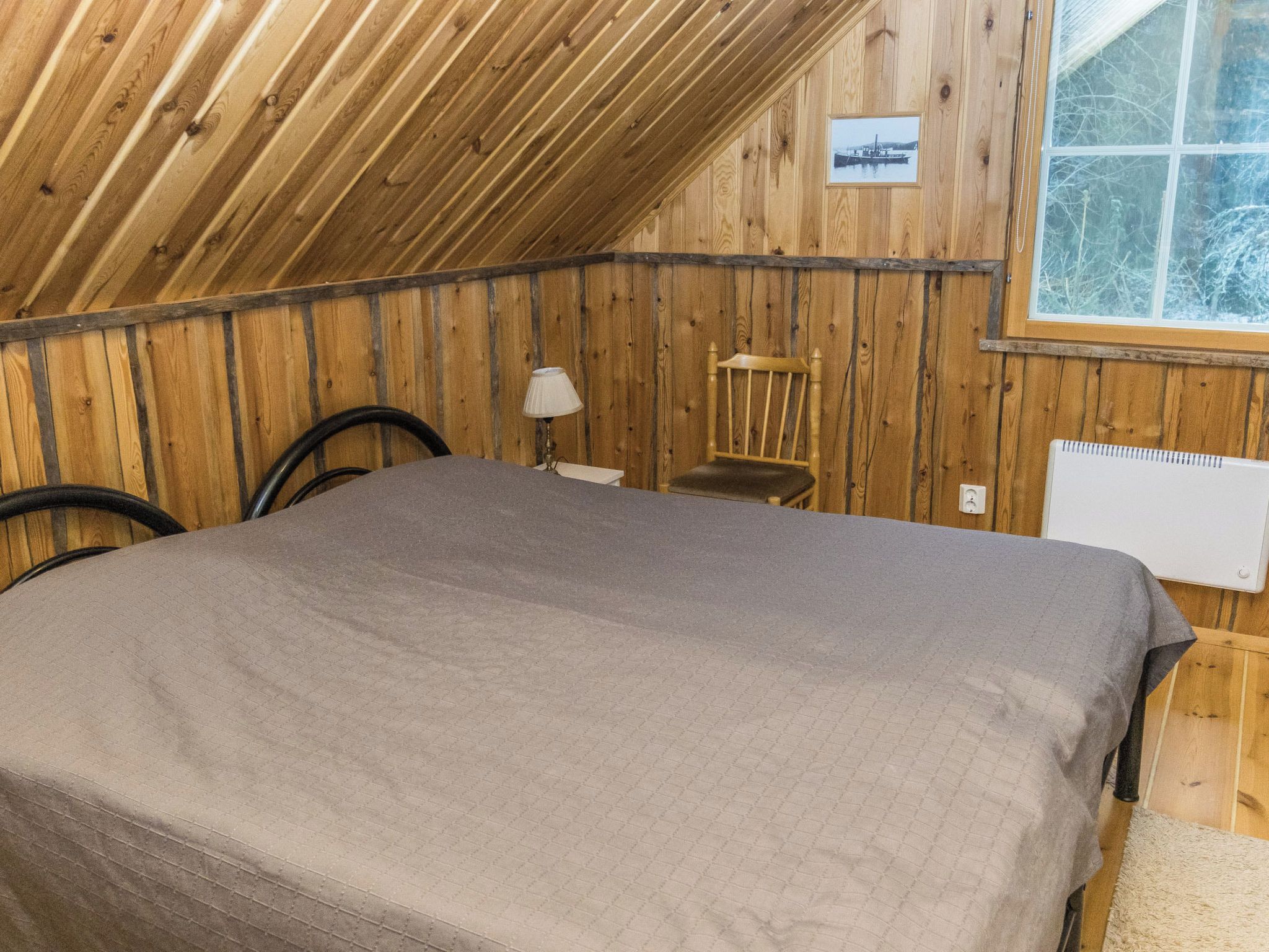 A room with a bed, a chair, a lamp, and a window.