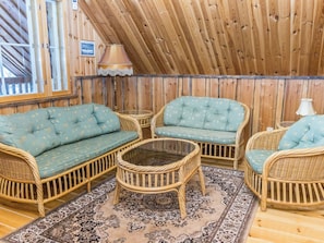 A cozy room with wooden walls and a sloped ceiling. There are two sofas and a round table with a glass top. A patterned rug is on the floor. - Kaislaranta by Interhome (Salo)