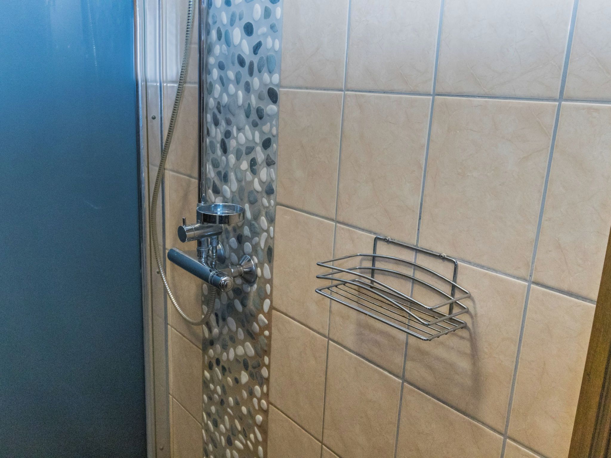 En dusch med en glasdörr, ett duschmunstycke i metall och en metallhylla på väggen.