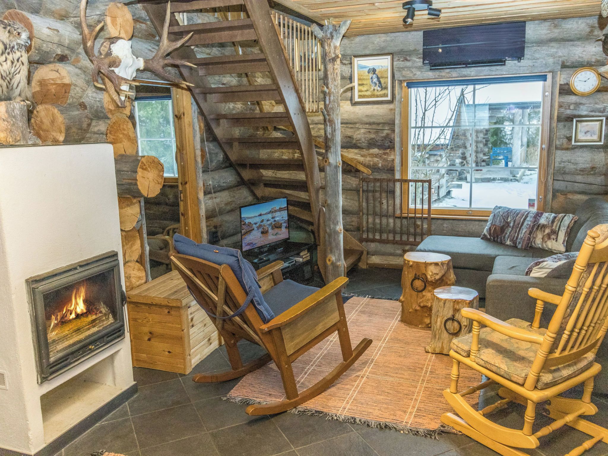 L’intérieur d’un chalet accueillant, avec une cheminée, un fauteuil à bascule en bois, un canapé et un téléviseur.
