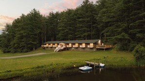 Una cabaña con muelle y barcos, rodeada de un bosque denso.