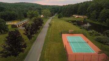 Camp de tennis al costat d'un edifici amb vista a un llac i a les colines boscoses.