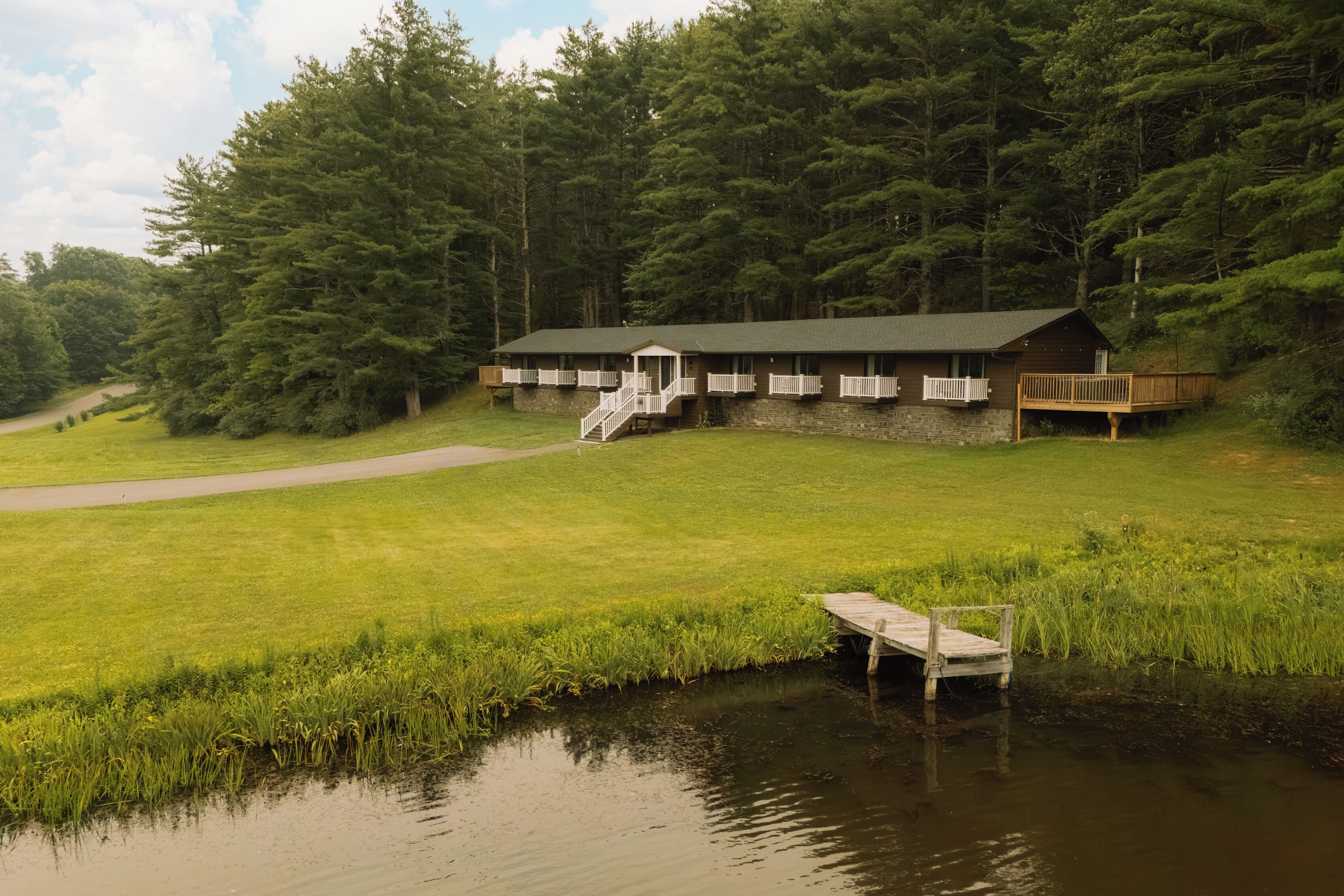 A lodge with a dock, surrounded by a grassy field and dense forest.