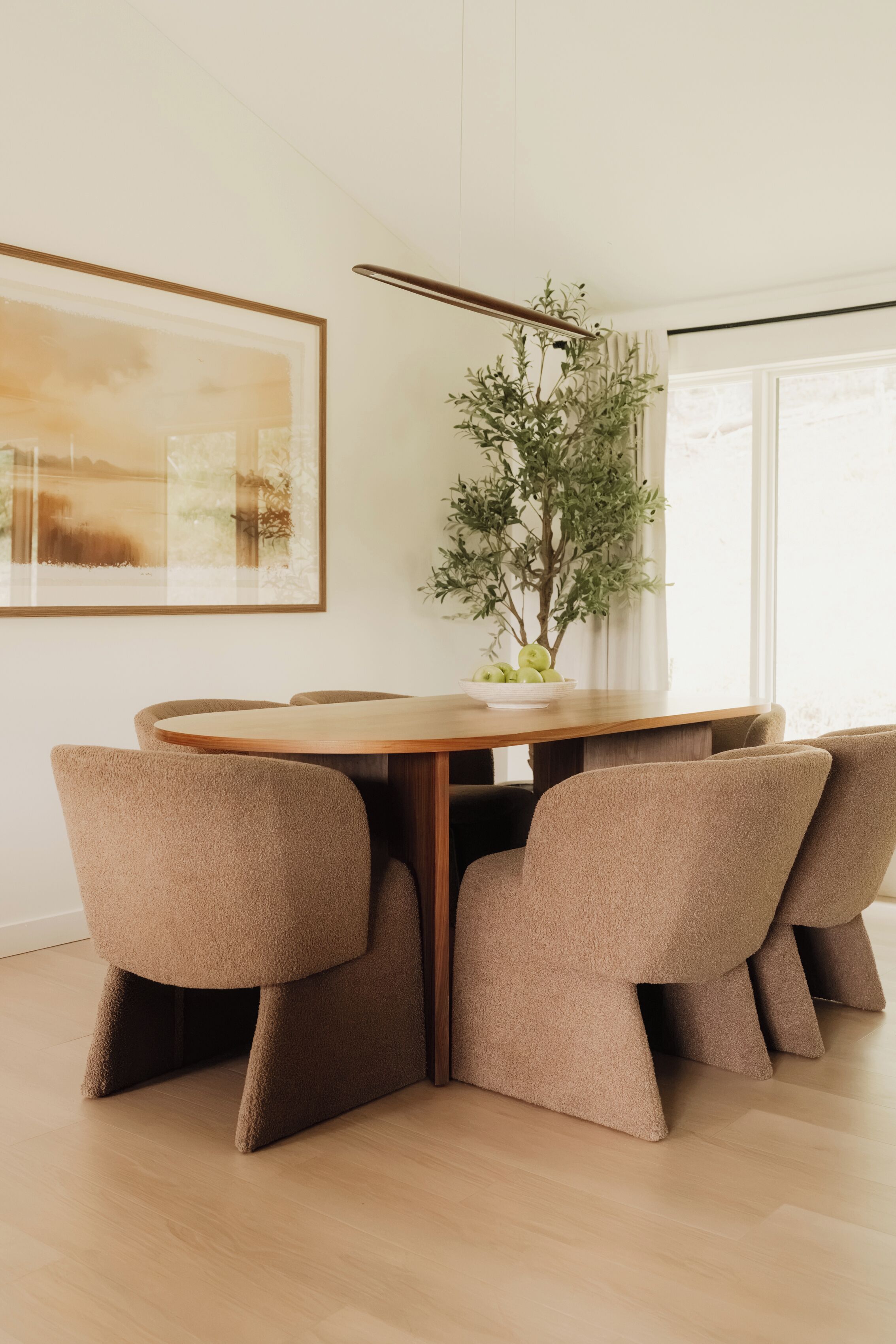 Un coin repas comprenant une table en bois, quatre chaises rembourrées, une plante en pot et une œuvre d’art encadrée accrochée au mur.