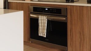 Una cocina moderna con armarios de madera, horno de acero inoxidable y encimera blanca.