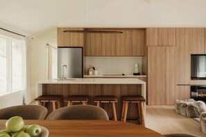 A modern kitchen with wooden cabinets, a stainless steel refrigerator, and a bar area with stools. - Pond House at Carter Bridge Estate (Freehold)
